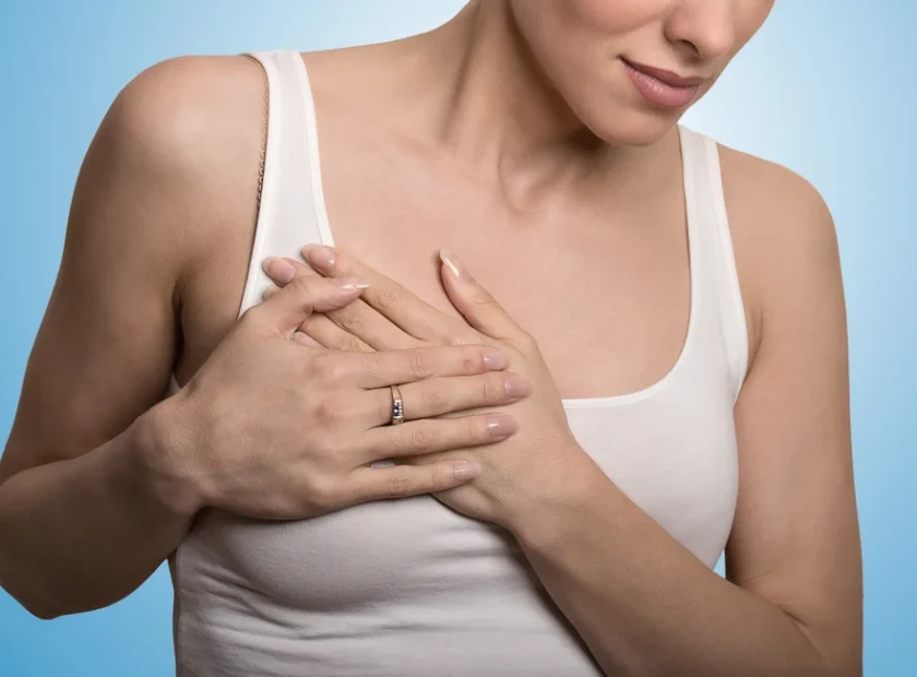 Closeup cropped portrait young woman with breast pain touching chest colored isolated on blue background