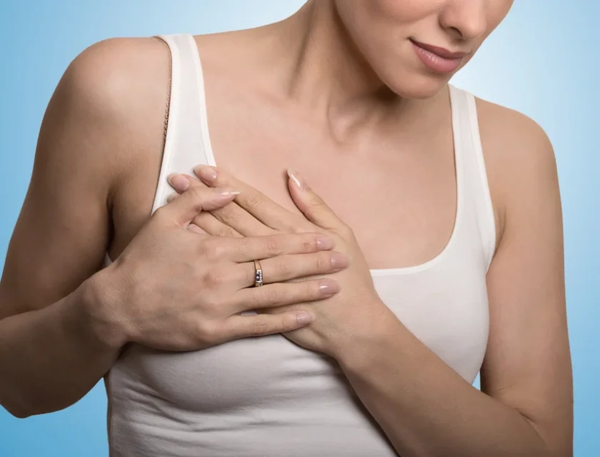 Closeup cropped portrait young woman with breast pain touching chest colored isolated on blue background